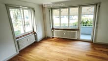 Empty room with wooden flooring, large windows, radiators, and a sliding glass door leading to a balcony.