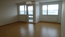 Empty room with wooden flooring, white walls, large windows, and a sliding glass door leading to a balcony.