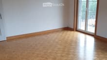Empty room with wooden herringbone flooring, white walls, and large sliding glass doors leading to a balcony.