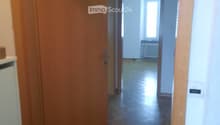 A narrow hallway with wooden doors, tiled floor, and a visible room at the end with a radiator and window.