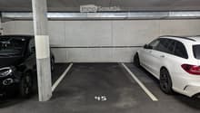 Underground parking area with two parked cars, marked parking spaces, and concrete pillars.