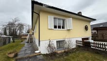 Raised ground floor, yellow and white painted house, white shutters, gravel pathway, fenced garden, chimney, metal railings on staircase
