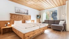 Cozy bedroom with wooden bed, nightstand, sofa, and TV, featuring large windows with a scenic view.