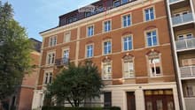 Four-story brick building with multiple windows, decorative balconies, and ornate wooden doors at the entrance.
