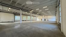 Large, empty industrial-style space with concrete floors, white walls, exposed ceiling beams, and large windows allowing natural light.