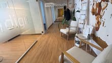 Modern hallway with wooden flooring, glass walls, and a seating area featuring a chair, small table, and plant.