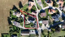 Aerial view of a residential area with multiple houses, gardens, driveways, and surrounding greenery.