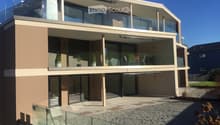 Modern two-story house with large glass balconies, beige and brown exterior, and a raised ground floor.