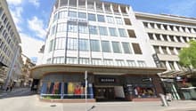 Modern multi-story building with large windows and a curved facade, featuring commercial storefronts at the ground level with signage for 'Globus' and other businesses.