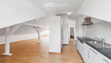 Bright, open kitchen and living area with white walls, wooden flooring, and modern kitchen cabinets.