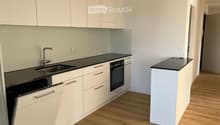 Modern kitchen with white cabinets, black countertops, a sink, and an oven. The floor is wooden.