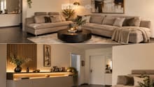 Modern living room with a large sectional sofa, coffee table, floor lamp, and decorative items including vases and picture frames. The space features warm lighting and a sleek design.
