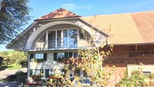 Two-story house with a large arched balcony, green shutters, and a well-maintained garden.