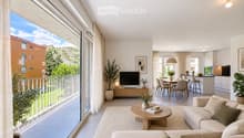 Modern, open-concept living and dining area with large windows offering a scenic view, featuring a beige sofa, wooden coffee table, flat-screen TV, dining table with chairs, and a sleek kitchen island.