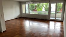 Empty room with wooden flooring, large windows, and sliding glass doors leading to a balcony.