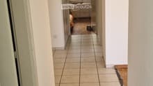 A long, narrow hallway with tiled flooring and white walls, leading to a room with a small table and chair visible at the end.