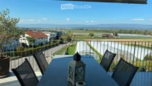 Balcony with a table, chairs, and a lantern, overlooking a rural landscape with fields and houses.