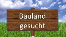 Wooden sign in a field indicating that 'Bauland' (land) is 'gesucht' (wanted)