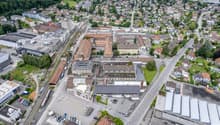 urban landscape with houses, roads, and buildings. A central area with several buildings, surrounded by other structures, including residential homes, commercial properties, and industrial facilities. Green areas, including lawns and trees, are scattered