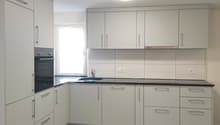 modern kitchen with white cabinets, black countertops, built-in oven, sink, and dishwasher