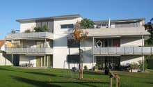 White two-story house, two balconies, green lawn, play equipment