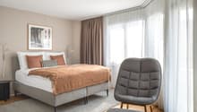 bedroom with bed, bedside tables, picture frame, curtains, chair, ottoman, carpet