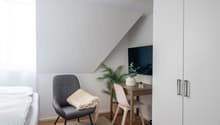 small room with bed, chair, desk, plant, and TV