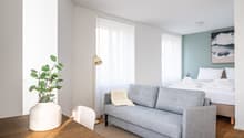A small room with a bed, a couch, a table, a plant, and a lamp.