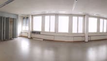 Large open office space with multiple windows, built-in shelving units, and a curved seating area along the wall.