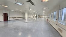 Long empty hall, white walls and ceiling, industrial style, multiple columns, windows on one side, fire extinguisher.