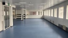 Empty room, white walls, blue floor, many windows, air vents on the walls
