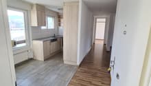 Empty hallway with wooden floor, white walls, kitchen with sink, cabinets, and dishwasher