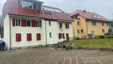 Two-story house with red roofs and windows, solar panels, brick driveway, bicycles parked