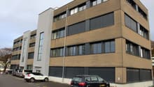3 story modern office building, brown exterior, windows, parking area