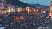 A large, crowded town square at night with brightly lit buildings and a large gathering of people