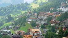 Mountain village with many houses, green hills, trees, and a mountain in the background