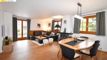 Spacious open-plan living area with hardwood floors, white walls, large windows, black leather sofa, wooden dining table and chairs, fireplace, and decorative lighting fixtures