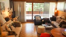 Spacious living room with large windows overlooking a balcony, hardwood floors, comfortable sofas and armchairs, coffee table, and various decorative elements.