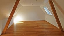 Spacious attic room with wooden beams, hardwood flooring, and a skylight window providing natural light.