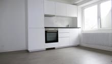 modern kitchen with white cabinets, black oven, white tiled backsplash, white radiator, wooden floor