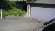 concrete building with a garage door, concrete barrier, small garden with green bush