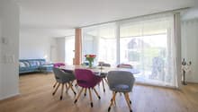 Dining room with wooden floor, large glass windows, dining table, and colorful chairs