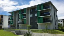 modern apartment building, green and gray exterior, multiple balconies, concrete fence, green lawn