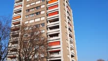 A tall residential building with multiple floors, balconies with orange shutters, and a beige and white exterior.