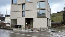 modern design multi-level building, grey concrete walls, glass windows, several trash bins, fenced area, street sign