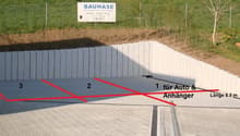 a sloped area with a concrete barrier for car and bicycle parking, a green grass field, and a white fence