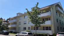 4 story apartment building, beige exterior, white balconies, street view, cars parked