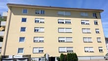 4 story building, beige exterior, white windows, small garden, trash bins, car parked