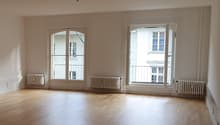 large empty room, wooden floor, three large windows with doors, radiators on the wall, white walls