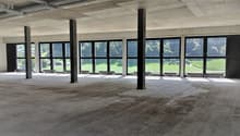 A wide empty room with many windows, two long benches, and pillars